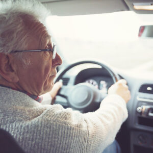 Friendly old gentleman with metal frame glasses drives car